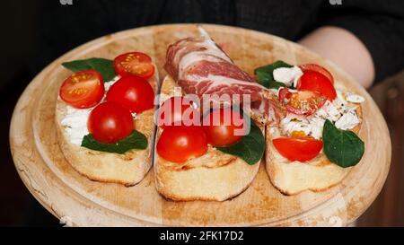 Cameriera donna che tiene in lei un vassoio di legno con bruschetta mano Foto Stock