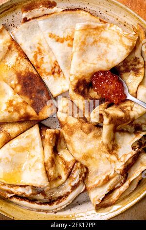 Sottili panscake crepe suzette servita con caviale rosso e burro fuso su piastra di ceramica. Vista dall'alto, primo piano Foto Stock