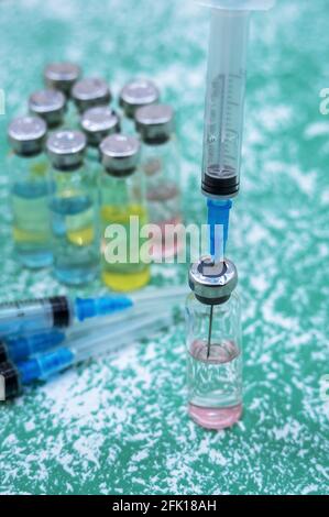 Prevenzione delle malattie stagionali. Fiale mediche, siringhe e una maschera su sfondo verde. Vaccinazione contro covid-19. Foto Stock