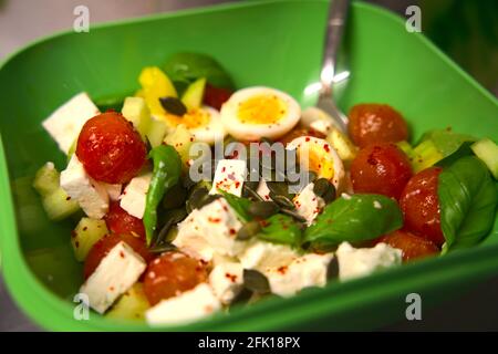 delizioso e colorato condimento di insalata fresca. servito in un recipiente di plastica verde con cucchiaio di metallo all'interno della ciotola, su sfondo neutro. Foto Stock