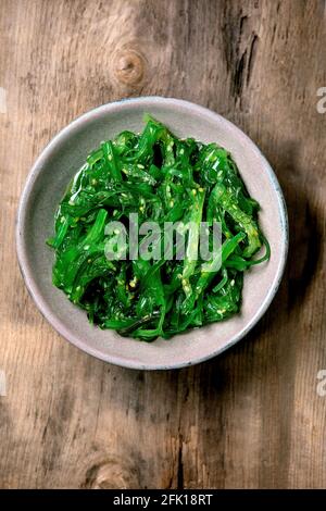 Insalata giapponese di alghe Wakame chuka con semi di sesamo in piastra di ceramica su vecchio sfondo di legno. Disposizione piatta, spazio di copia Foto Stock
