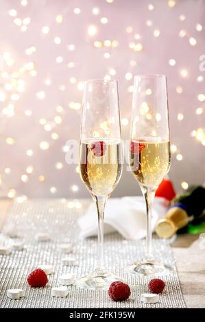 Biglietto d'auguri per San Valentino con due bicchieri di champagne lampone sul vassoio in piedi su un tavolo scintillante d'argento, cuori bianchi, luci bokeh. Tavolo festivo Foto Stock