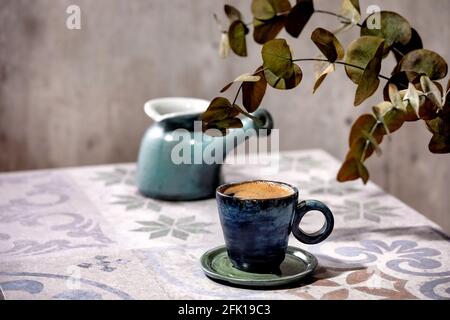 Tazza di caffè nero turco sul tavolo ornato in ceramica con cezve di caffè e rami di eucalipto. Luce solare Foto Stock