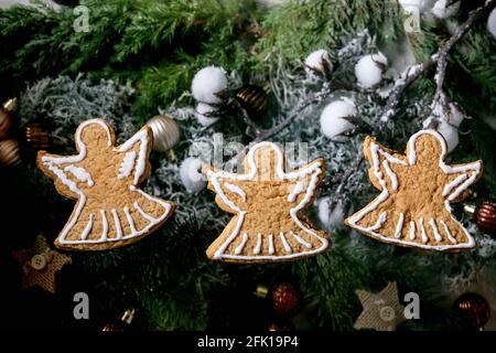Biscotti fatti in casa con pan di zenzero natalizio con glassa ornata. Tre angeli di pan di zenzero con decorazioni xmas e abeti come sfondo. Piatto Foto Stock