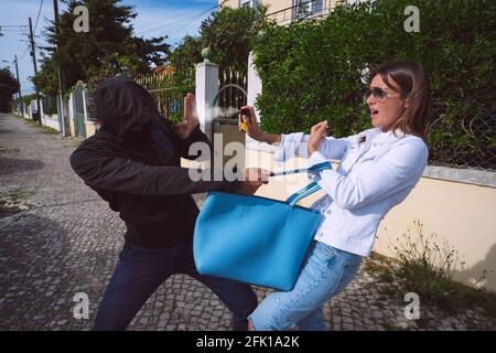 Ladro cercando di rubare la borsa della donna. Donna che usa lo spray al pepe per autodifesa Foto Stock