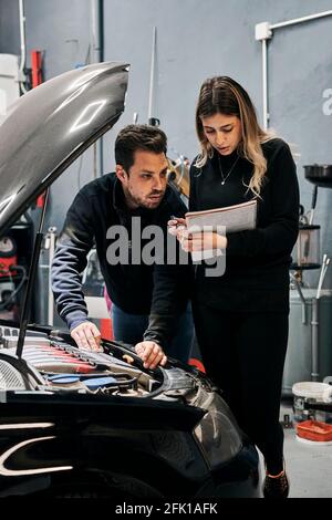 Due meccanici si aiutano a vicenda nel lavoro di a. garage Foto Stock