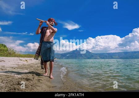 Un uomo che suona uno strumento musicale distillato sulle rive del lago Toba Foto Stock