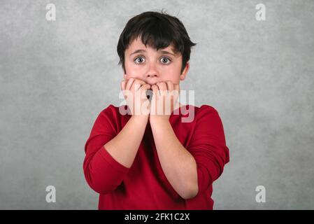 capretto spaventoso che morde le sue unghie su uno sfondo grigio Foto Stock