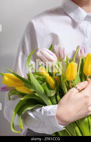 Donna in camicia bianca contiene bouquet di giallo e rosa tulipani nelle mani Foto Stock