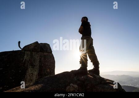 Silhouette di uomo in piedi sulla cima di montagna rocciosa vicino al tramonto ora Foto Stock