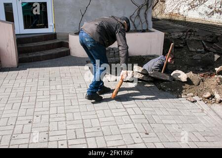 Dnepropetrovsk, Ucraina - 03.26.2021: Un lavoratore spazza su sporcizia dopo la sostituzione dei tubi fognari. Foto Stock