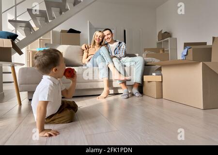 Felice coppia di famiglia con figlio di bambino che si rilassa durante il giorno in movimento in un nuovo salotto di casa. Foto Stock