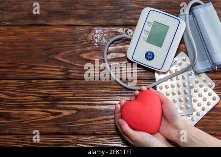 Tonometro elettrico bianco, cuore rosso e pillole, su tavolo di legno. Foto Stock