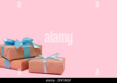Pila di scatole regalo davanti a sfondo rosa pastello. Presente con nastro legato blu. Concetto festivo con copyspace. Foto Stock