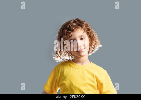 Adorabile bambino di 5 anni in T-shirt gialla in posa su grigio Foto Stock