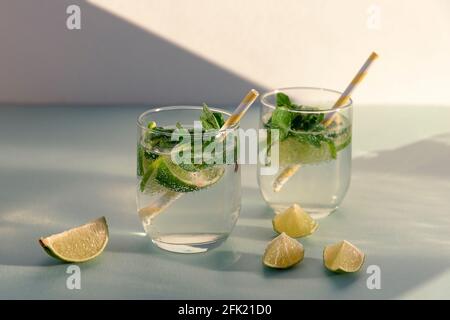 Due bevande mojito con la paglia sul tavolo blu, fette di lime. Bevande rinfrescanti fredde contro le pareti bianche alla luce del sole. Foto Stock