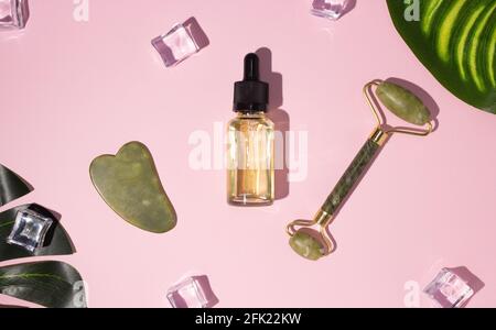 Raschietto Jade gua sha, massaggiatore facciale a rulli e olio cosmetico con foglia di monstera. Il concetto di self-care. Cura del viso. Zero sprechi. Sollevamento e tonin Foto Stock