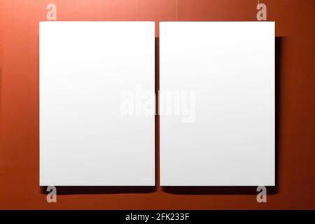 Due poster bianchi vuoti con area per la copia sono appesi su una parete rossa. Vista frontale, foto di sfondo Foto Stock