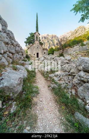 Un percorso murato in pietra che conduce al piccolo disusato 1000 Chiesa di un anno, in alto accanto alle mura di San Giovanni Fortress.set tra i bei montai Foto Stock