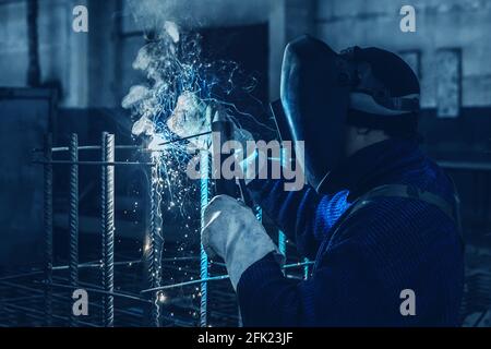 L'uomo che lavora sta svolgendo lavori di saldatura su strutture metalliche in una fabbrica o in un'impresa industriale. Foto Stock