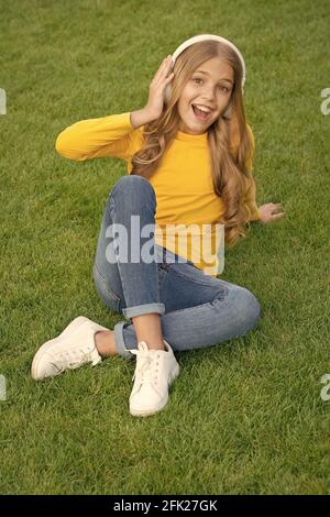 playlist di primavera. happy little girl ascolta la canzone preferita. kid beauty fashion. teen girl ascolta musica. suoni della natura. relax su erba verde Foto Stock