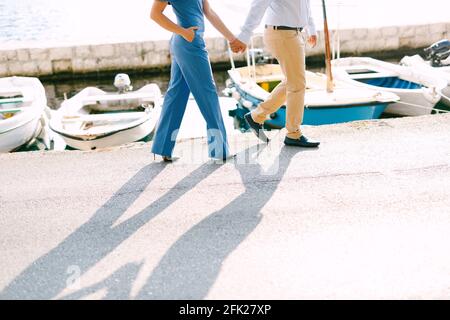 L'uomo e la donna camminano lungo il molo tenendo le mani sullo sfondo di yacht in una giornata di sole Foto Stock