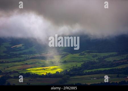 Luce solare brillante attraverso il buco di nuvole a oscura scena di catena montuosa, Azzorre, Sao Miguel, Portogallo. Il fascio di luce attraverso la nuvola scura Foto Stock