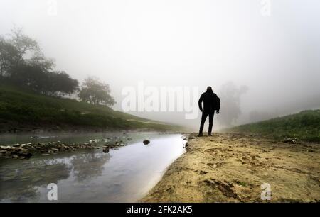 Vista posteriore di un giovane maschio con uno zaino in piedi dal flusso Foto Stock