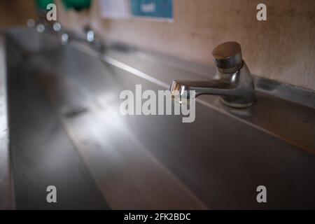 Vista prospettica di un lavabo pubblico. Primo piano di un rubinetto. Messa a fuoco in primo piano. Foto Stock