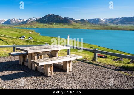 Tavolo da picnic vuoto in legno che si affaccia su un maestoso paesaggio costiero con montagne sullo sfondo in una giornata estiva soleggiata Foto Stock