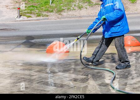 Un giubbotto in una camicia blu lava la pavimentazione con un tubo spray. Foto Stock