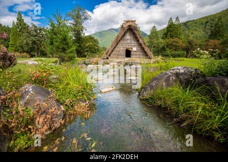 Piccola casa tradizionale giapponese vicino al fiume. Edificio con tetto di paglia. Ogimachi Shirakawa-go, un sito patrimonio dell'umanità dell'UNESCO. Shirakawa, Giappone Foto Stock