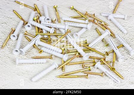 Molti tasselli in acciaio e plastica per la riparazione su fondo cementizio grigio chiaro. Fai da te, miglioramento della casa e concetto di costruzione della casa. Foto Stock