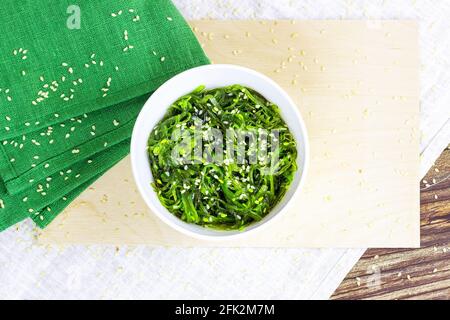 Vista dall'alto dell'insalata verde di alghe asiatiche in una ciotola bianca su sfondo di legno. Foto Stock