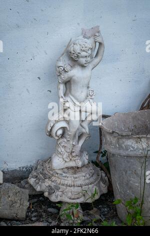 Statua di un piccolo Angelo rotto accanto alla spazzatura Foto Stock