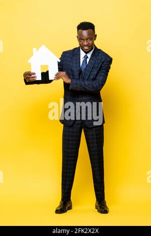 Giovane uomo d'affari africano come agente immobiliare holding house modello ritagliato su sfondo giallo isolato Foto Stock