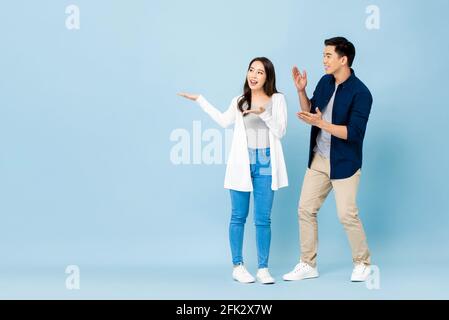 Sorridi eccitati turisti asiatici coppia indicando le mani allo spazio vuoto da parte su sfondo blu chiaro isolato Foto Stock