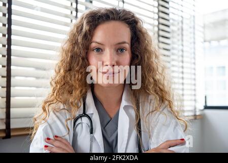 Sorridente medico femminile che guarda la fotocamera mentre fa la videochiamata in linea, concetti di servizio di consulazione medica domestica Foto Stock