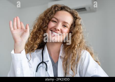 Giovane donna medico agitando la mano saluto paziente online tramite videochiamata, concetti di servizio di consulenza medica a casa Foto Stock