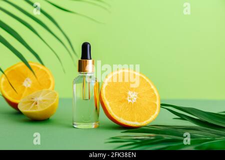 Siero cosmetico Vitamina C in flacone di vetro con contagocce per pipette. Olio essenziale arancio con ingredienti di agrumi Vitamina C e foglie di palma di colore verde Foto Stock