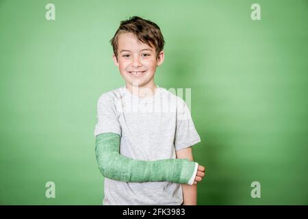 giovane scolaro fresco con braccio rotto e intonaco verde in posa davanti a sfondo verde Foto Stock