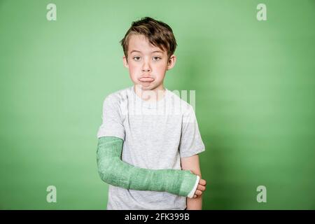 giovane scolaro fresco con braccio rotto e intonaco verde in posa davanti a sfondo verde Foto Stock