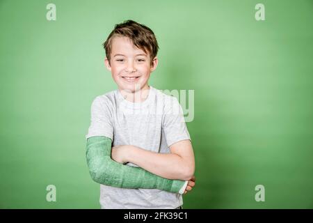 giovane scolaro fresco con braccio rotto e intonaco verde in posa davanti a sfondo verde Foto Stock