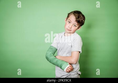 giovane scolaro fresco con braccio rotto e intonaco verde in posa davanti a sfondo verde Foto Stock