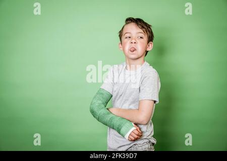 giovane scolaro fresco con braccio rotto e intonaco verde in posa davanti a sfondo verde Foto Stock