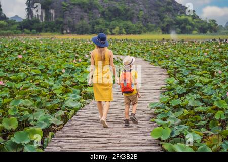 Madre e figlio in giallo sul sentiero tra il lago di loto. MUA Cave, Ninh Binh, Vietnam. Il Vietnam riapre dopo la quarantena Coronovirus COVID 19 Foto Stock