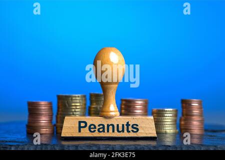 Germania. 27 Apr 2021. Un francobollo in legno con l'iscrizione 'Peanuts' davanti a diverse pile di monete euro/centesimi su una piastra di ardesia lucida. Foto con composizione su sfondo blu. Le arachidi sono colloquialmente un'espressione per le piccole cose o le somme insignificanti di soldi. La parola è stata dichiarata la parola tedesca dell'anno 1994 | Usage worldwide Credit: dpa/Alamy Live News Foto Stock