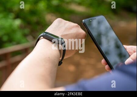 Primo piano di mani maschili che tengono lo smartwatch e lo smartphone sul passeggiata Foto Stock