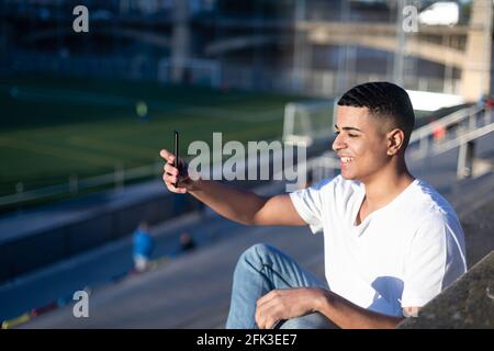 Un giovane bell'uomo in t-shirt e jeans si siede sopra uno stadio sbiancante da solo Foto Stock