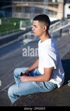 Un giovane bell'uomo in t-shirt e jeans si siede sopra uno stadio sbiancante da solo Foto Stock